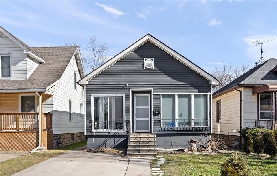 Dark grey sided detached bungalow at 374 Rankin Avenue, Windsor, with an enclosed front sunroom, central entrance with steps, and a concrete driveway to the left.